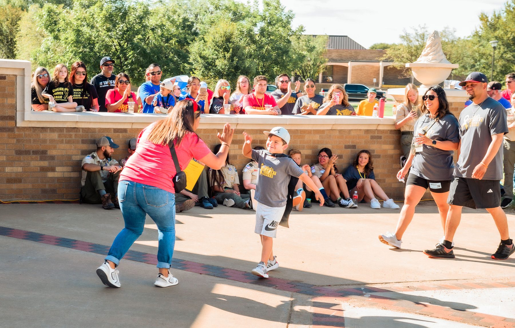 A boy runs toward a volunteer with his arms out while a crowd cheers behind them at the Lubbock Pediatric Cancer Walk.